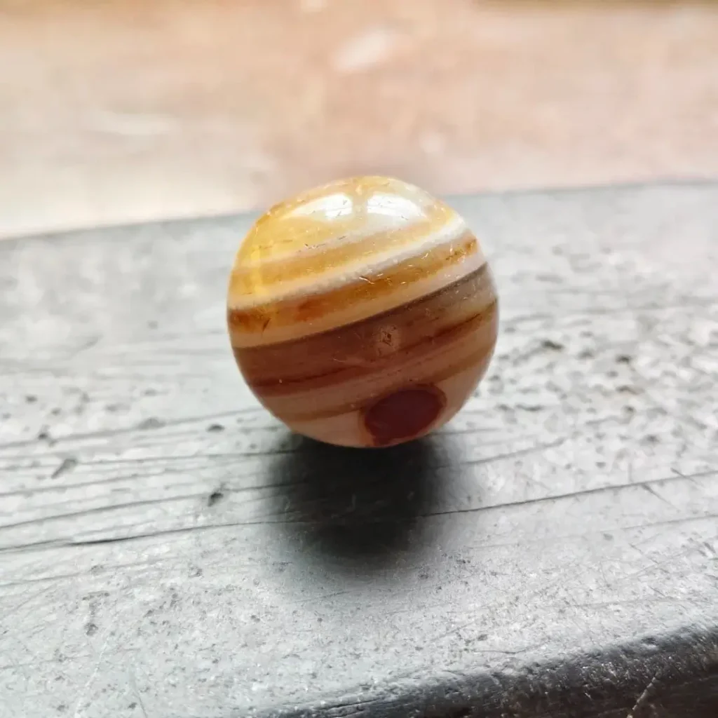 Ancient Iranian banded agate bead showing colorful layered spiral patterns.
