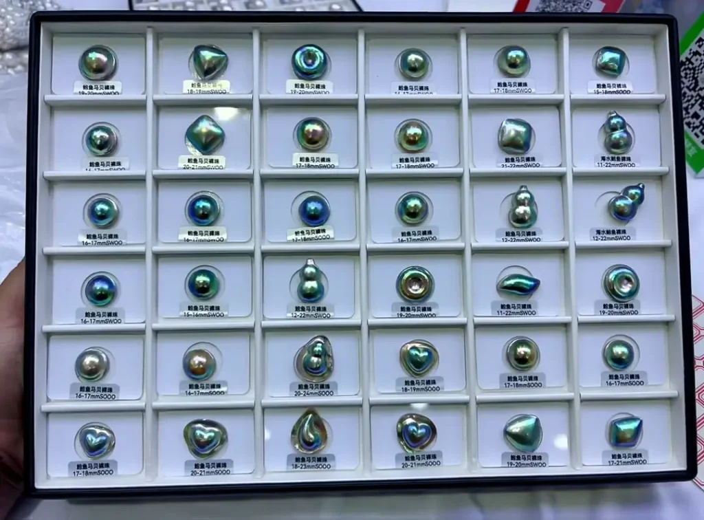A display tray filled with iridescent pearls in green, blue, purple, and organic shapes.