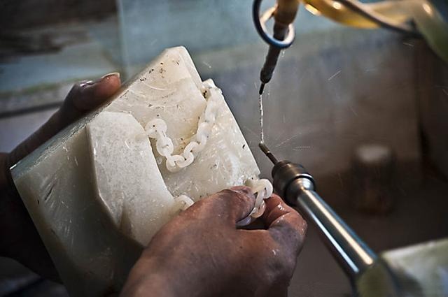 Artisan using a carving tool to hollow the inner openings of jade chain rings.
