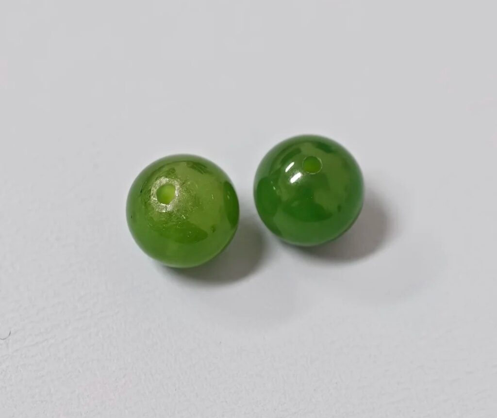 Two green jasper beads, one with edge chipping around the drill hole and one smooth and intact.