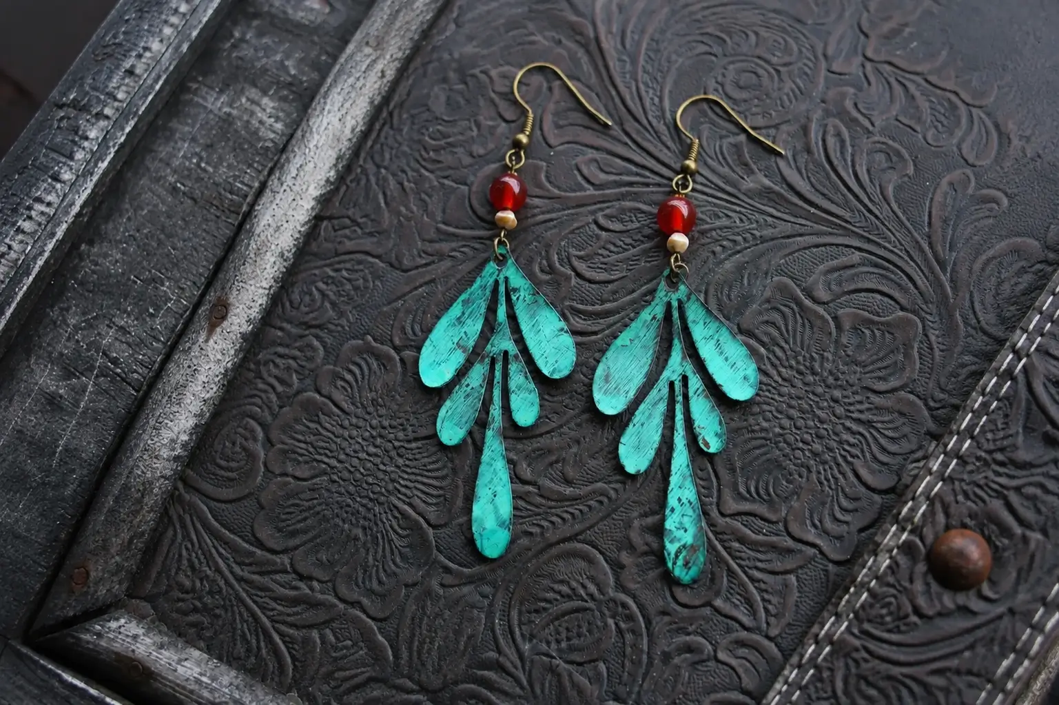 Openwork leaf-shaped patina brass earrings with green texture and red bead accents.