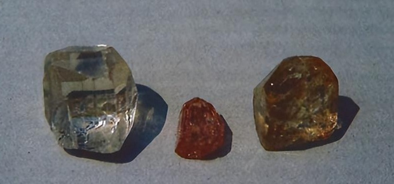 Three Pakistani Topaz crystals in colorless, pink, and brown hues on a grey background.