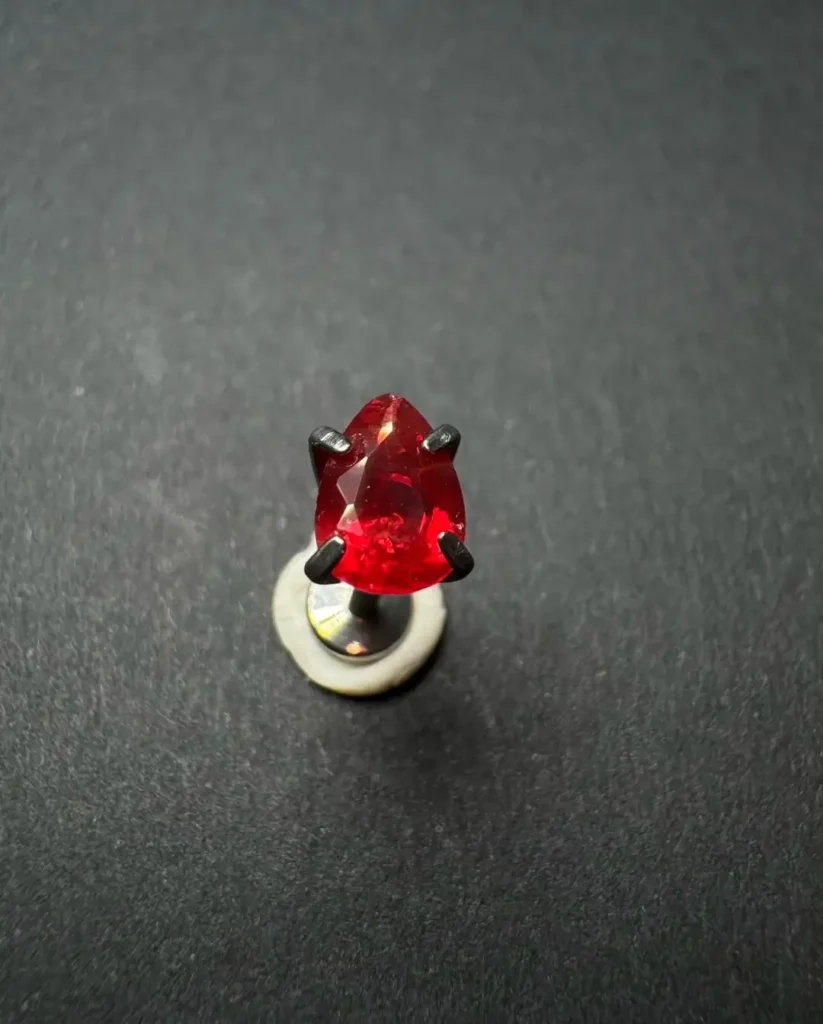 Pear-cut red Oregon Sunstone ear stud with vivid red color in a dark metal setting.