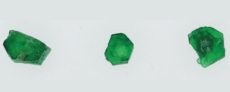 Three green Swat Emerald rough crystals displayed on a white background.
