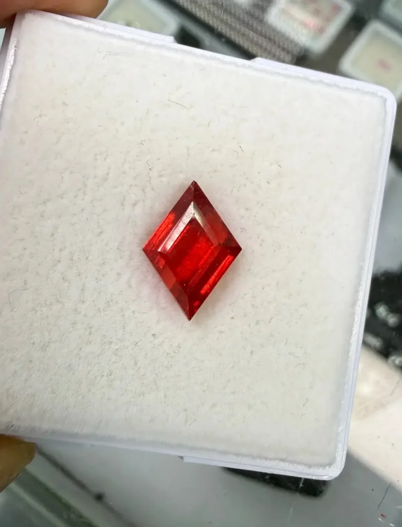 Vivid red rhodonite gemstone with a faceted rhombus cut and a ruby-like red color.