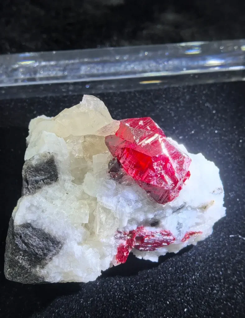 Translucent bright-red crystal on a white mineral matrix.