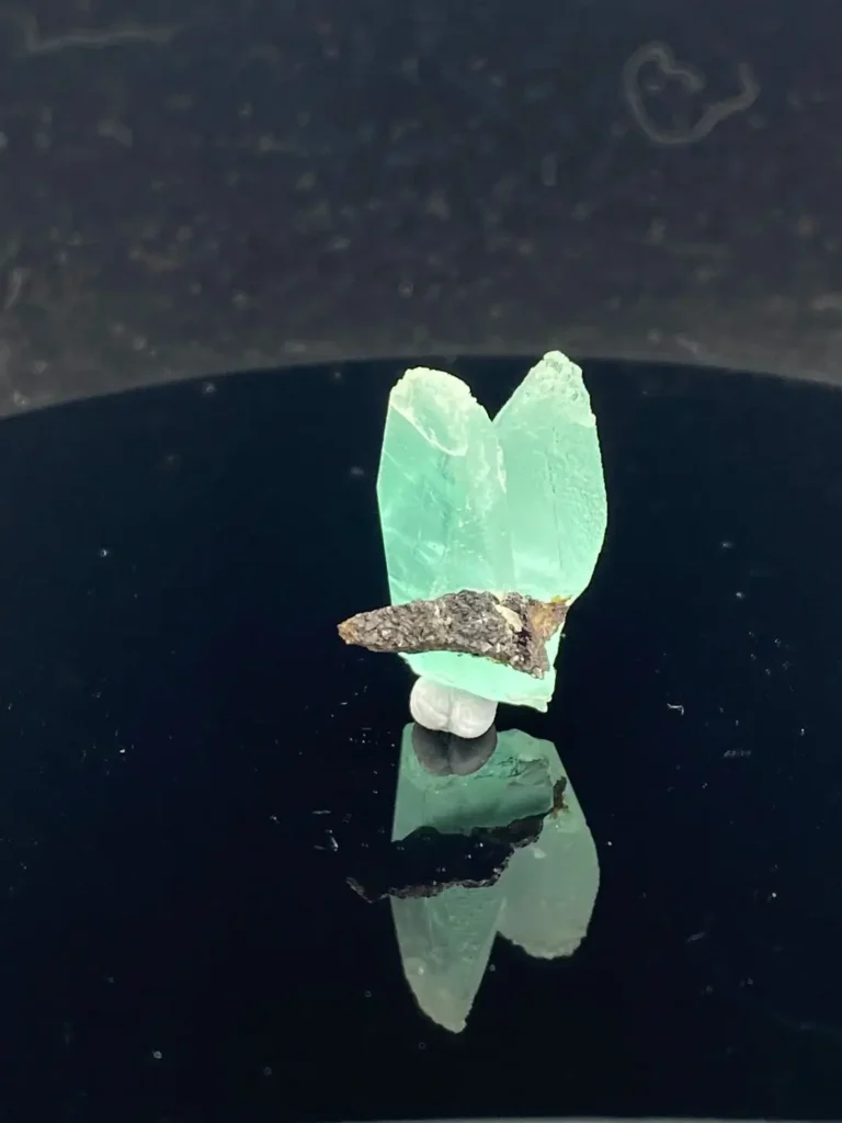 16.8 ct pale blue-green phosphophyllite twin specimen with some surrounding matrix.