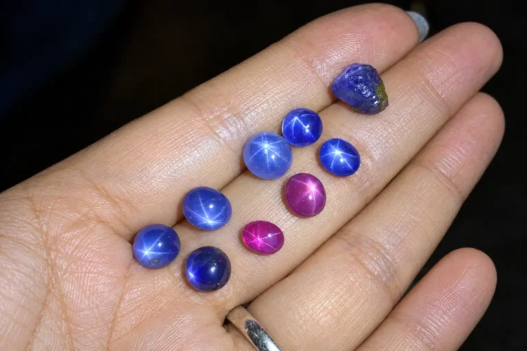 Blue and purple star sapphires displayed in a palm, each showing a distinct six-rayed star.