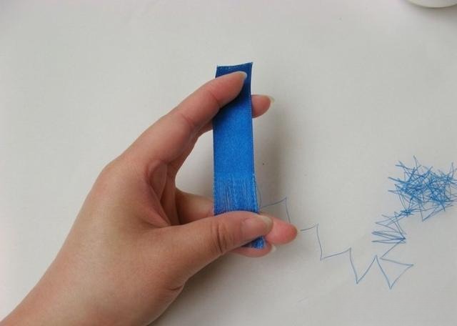 Hands pulling individual threads from blue satin ribbon for a faux Diancui tutorial.