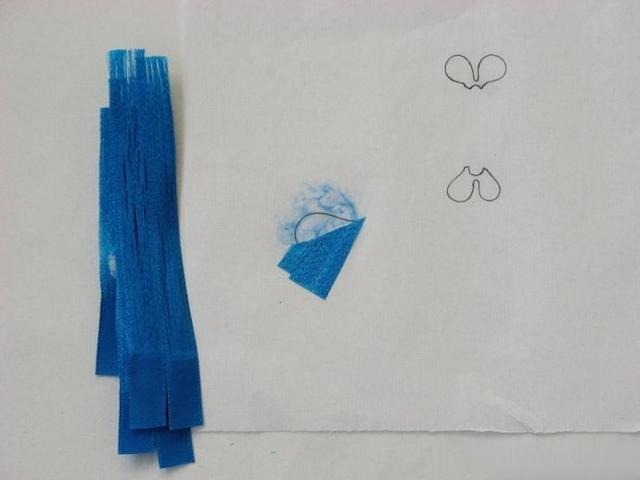 Blue ribbon strands glued onto a small paper template to form a feather-inspired pattern.